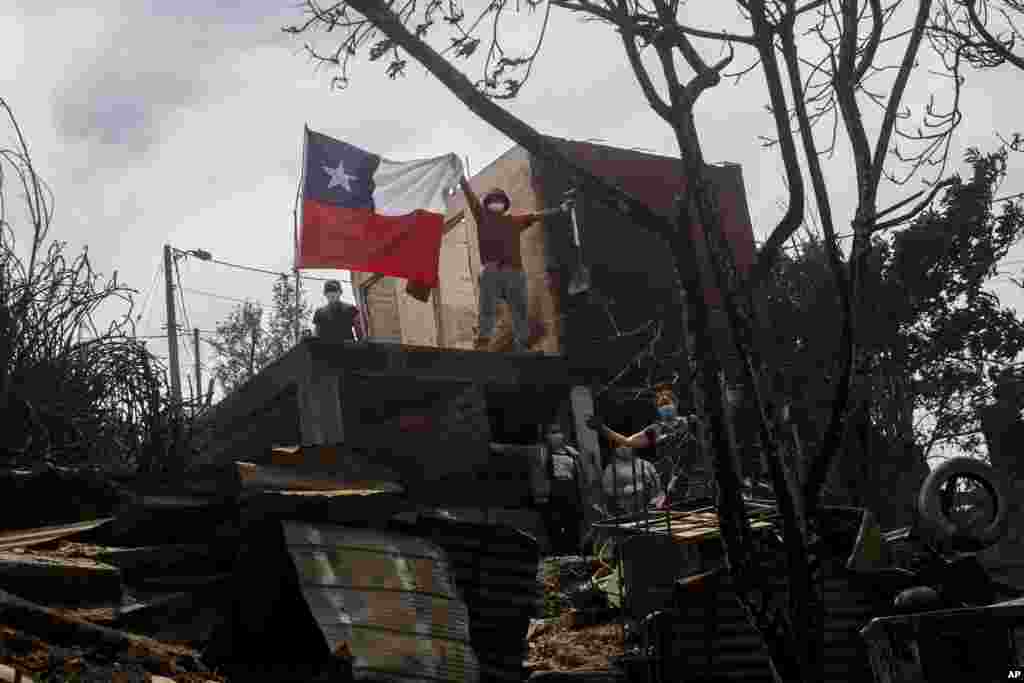 Un residente muestra una bandera chilena desde una casa incendiada después de que los incendios forestales alcanzaran su barrio. 