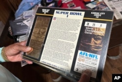 Gregory Eaton holds up a ticket and other items related to the first Super Bowl at his home, in Lansing, Michigan, Jan. 30, 2024.