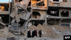 Palestinos desplazados caminan frente a un edificio destruido en un bombardeo israelí en Khan Yunis, en el sur de la Franja de Gaza, el 15 de mayo de 2024.