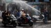 Orang-orang dengan skuter lewat di bawah alat penyiram air di bawah terik matahari pada saat musim panas di Ahmedabad, India, 9 Mei 2024. (Foto: Reuters)