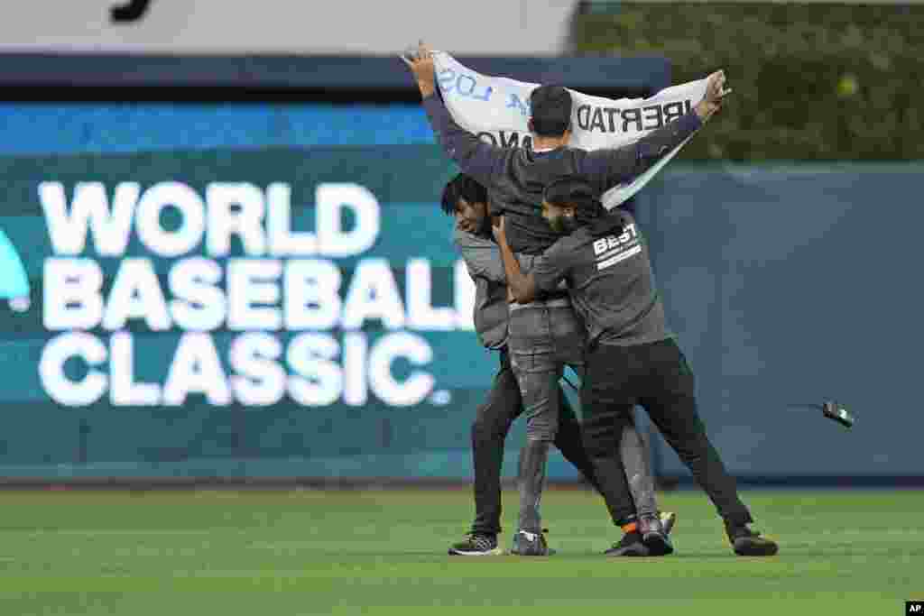 Guardias de seguridad sacan a un manifestante que ingresó al campo durante la sexta entrada del Clásico Mundial de Béisbol entre Cuba y Estados Unidos.