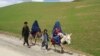 Mujeres afganas vestidas con burka montan en burro junto a niños en una carretera cerca de la aldea de Shah Mari en el distrito de Argo, provincia de Badakhshan, Afganistán, el 1 de mayo de 2024.