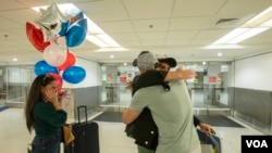 Edeitys Elián Coto Sierra mira a su hermano, Maikel Antonio Coto Salazar, de Cuba, quien llegó a Miami a través del programa de parole humanitario, y abraza a su amigo Yasser Dughman Cabrera, el viernes 17 de marzo de 2023. Foto: Alexia Fodere para Voz de América. 