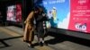 FILE - Two women look at a mobile phone in front of billboards at a bus stop in Beijing, China, Nov. 11, 2023.