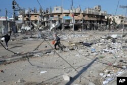 Palestinos caminan entre la destrucción causada por el bombardeo israelí en el campo de refugiados de Nuseirat en la Franja de Gaza, el martes 16 de enero de 2024. (Foto AP/Adel Hana)