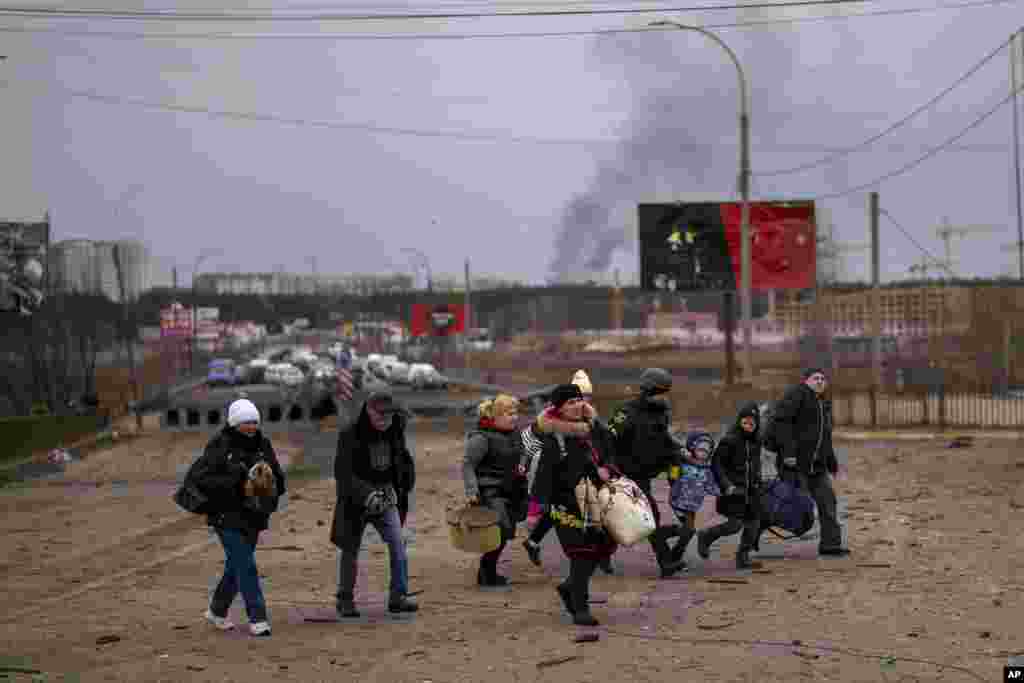 Un oficial de policía ucraniano ayuda a las personas mientras la artillería resuena cerca mientras huyen de Irpin en las afueras de Kiev, el 7 de marzo de 2022. Rusia anunció otro alto el fuego y varios corredores humanitarios para permitir que los civiles huyan de Ucrania.