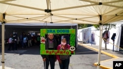 Una pareja posa para una foto sosteniendo un marco con un mensaje que dice: "Tercera dosis, vacúnese, refuerzo", luego de recibir un refuerzo de AstraZeneca durante una campaña de vacunación para personas de 60 años y más, en Ciudad de México, el 4 de enero de 2022.