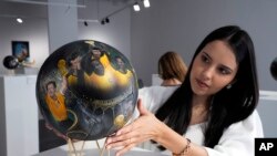 La artista paraguaya Lili Cantero observa uno de los balones que pintó, con la imagen del as brasileño Pelé, en una exposición en Katara Cultural Ville, en Doha, Qatar, el 24 de noviembre de 2022. (AP Foto/Jorge Sáenz)