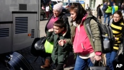 Refugiados ucranianos con niños abordan el transporte en una plaza junto a una estación de tren en Przemysl, Polonia, el martes 22 de marzo de 2022. [Foto AP/Sergei Grits]