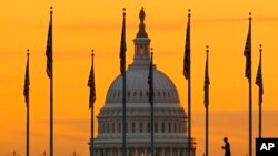 La silueta de un peatón temprano en la mañana contra el amanecer mientras camina frente a las banderas de EEUU en el National Mall y pasa por el edificio del Capitolio en Washington, el 7 de noviembre de 2022.