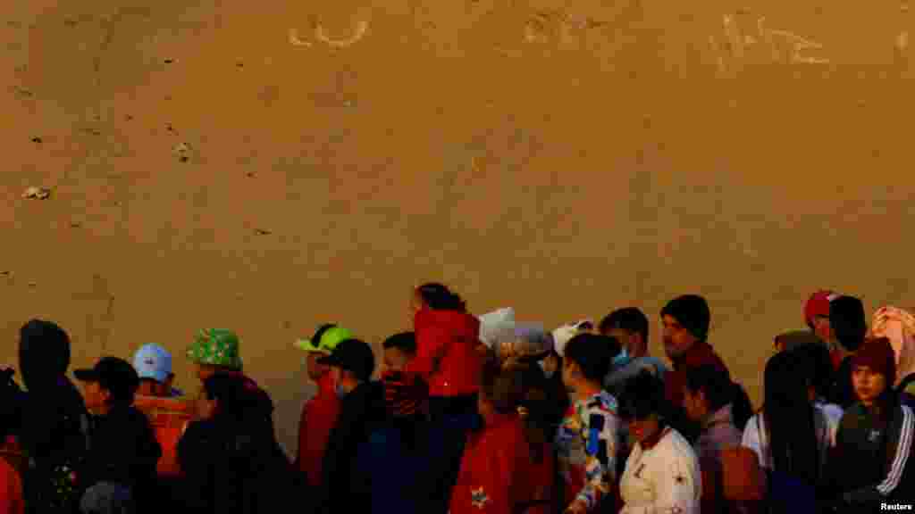Los migrantes hacen cola cerca del muro fronterizo después de cruzar el río Bravo para entregarse a los agentes de la Patrulla Fronteriza de EEUU para solicitar asilo en la ciudad estadounidense de El Paso, Texas.&nbsp;