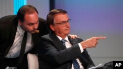 Carlos Bolsonaro, hijo del presidente de Brasil, Jair Bolsonaro, quien se postula para la reelección, susurra al oído de su padre durante su llegada al debate presidencial en Río de Janeiro, Brasil, el jueves 29 de septiembre de 2022. elecciones el 2 de octubre. (AP Photo/Bruna Prado)