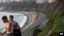 Con una carretera vacía de fondo, Liza Mell, de 26 años, y Jean-Marie Landre, de 27, ambos franceses que viven en Lima, caminan con mascarillas para protegerse del coronavirus, el sábado 21 de marzo de 2020, en Lima, Perú.