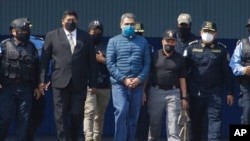 El expresidente hondureño Juan Orlando Hernández, centro, es llevado esposado a un avión en el que fue extraditado a Estados Unidos, desde una base de la Fuerza Aérea en Tegucigalpa, Honduras, el 21 de abril de 2022.