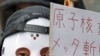 A protester wearing a mask holds a sign at a rally, in front of the headquarters of Tokyo Electric Power Company [TEPCO], aimed at criticizing TEPCO and demanding the abolition of nuclear power, in Tokyo, March 3, 2012. 