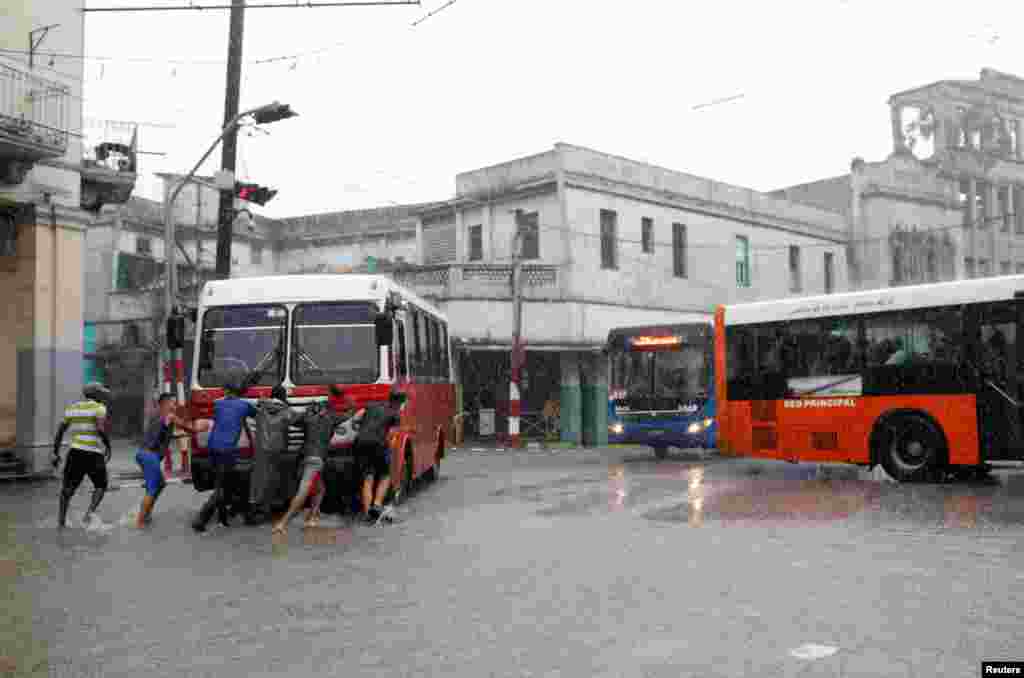 La gente empuja un autobús con fallas técnicas bajo las intensas lluvias en capital cubana.