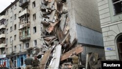 Los militares ucranianos se paran frente al apartamento de Valentina Popovichuk, donde fue rescatada después de un bombardeo ruso en un ataque militar, mientras continúa la invasión rusa de Ucrania, en Kharkiv, Ucrania, el 11 de julio de 2022.