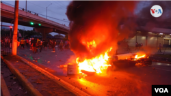 Manifestantes en medios de barricadas con fuego. [Foto: VOA]