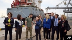 En esta foto proporcionada por la Oficina de Prensa Presidencial de Ucrania, el presidente de Ucrania, Volodymyr Zelenskyy, en el centro, rodeado de embajadores de diferentes países y funcionarios de la ONU, visita un puerto en Chornomork durante la carga de granos en un barco turco, al fondo, cerca de Odesa, Ucrania. Viernes, 29 de julio de 2022. (Oficina de Prensa Presidencial de Ucrania vía AP)