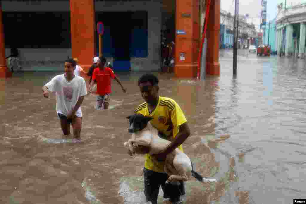 En La Habana, un hombre carga con su perro mientras cruza una calle bajo las fuertes lluvias.
