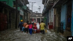 Voluntarios empujan a una mujer en un bote por una calle de un barrio inundada por fuertes lluvias, en La Habana, Cuba, el viernes 3 de junio de 2022. (AP Foto/Ramon Espinosa)
