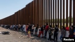 ARCHIVO - Migrantes que buscan asilo, en su mayoría de Venezuela y Cuba, esperan ser transportados por agentes de Aduanas y Protección Fronteriza de EE. UU. después de cruzar el río Bravo hacia EE.UU. desde México en Eagle Pass, Texas, el 14 de julio de 2022.