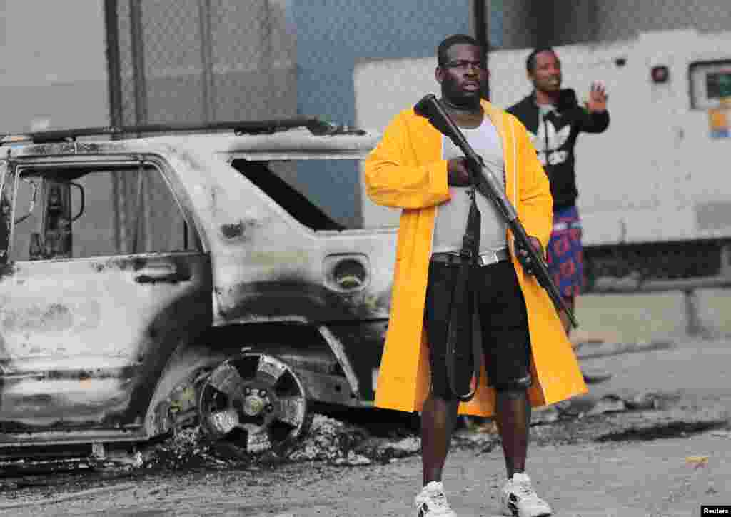 Un hombre armado se para cerca de un automóvil quemado durante las protestas que se sucedieron tras el anuncio del aumento de los precios del combustible, y el crimen avanza en el país. Imagen tomada en Puerto Príncipe, Haití, el 14 de septiembre de 2022.