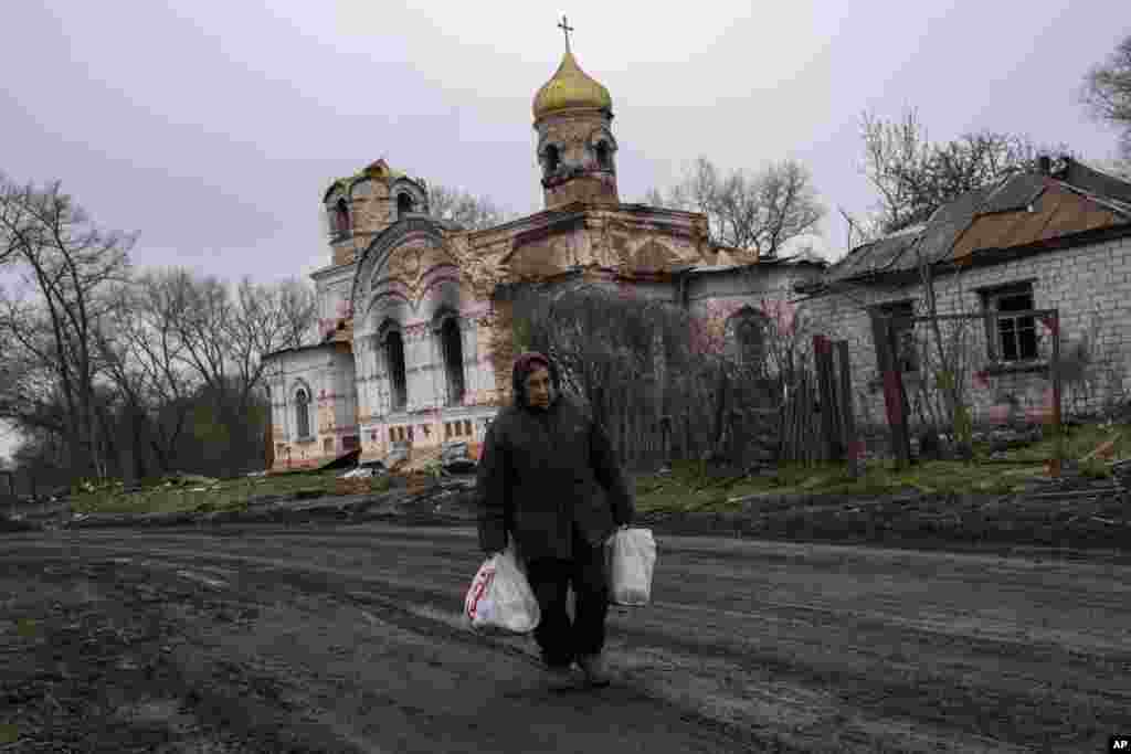 Valentyna Bushtruk, de 70 años, camina frente a una iglesia dañada en Lukashivka, en el norte de Ucrania, el viernes 22 de abril de 2022. Según los residentes, los soldados rusos utilizaron el templo para almacenar munición y las fuerzas ucranianas bombardearon el edificio para que los rusos se marcharan. (AP Foto/Petros Giannakouris)