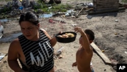 Andrea Calisti sostiene una bandeja de pan dulce donado mientras su hijo Natanael, de 7 años, alcanza un pedazo, en el barrio 17 de Octubre de Buenos Aires, Argentina, el 2 de febrero de 2022. 