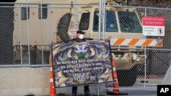 Un manifestante sostiene un cartel frente a la cerca fortificada y el vehículo de la Guardia Nacional que protege el Centro de Gobierno del condado de Hennepin, el 1 de abril de 2021, en Minneapolis.