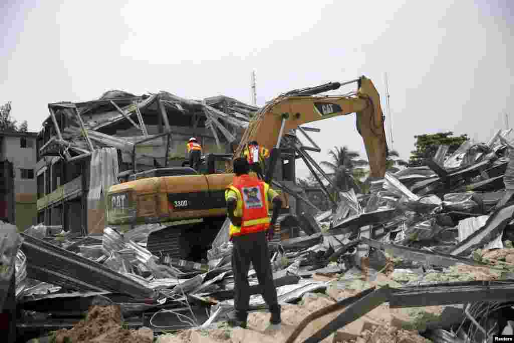 An emergency official watches an excavator dig through the rubble of a collapsed building in the Victoria Island district of Lagos, Nov. 5, 2013.
