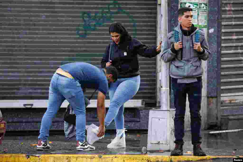 Un hombre pone bolsas de plástico en los pies de una mujer después de las lluvias causadas por un potencial ciclón tropical, que según el Centro Nacional de Huracanes de EEUU, probablemente se convertirá en la tormenta tropical Bonnie, a su paso por el Caribe, en Caracas, Venezuela.