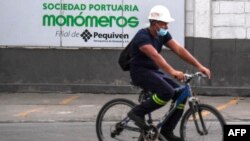 Un trabajador cpasa en bicicleta frente a un cartel de Monómeros Barranquilla, Colombia. [Archivo AFP]