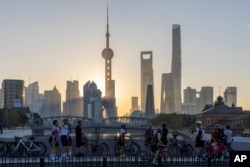 En esta foto publicada por la agencia de noticias Xinhua, ciclistas se toman selfies mientras descansan frente al horizonte del amanecer en Pudong, el centro financiero y comercial de China, en Shanghai, China, el viernes 3 de noviembre de 2023.