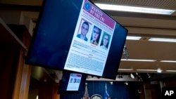 El ruso Yevgeniy Polyanin, buscado por el FBI, aparece en los monitores mientras el fiscal general Merrick Garland habla en una conferencia de prensa en el Departamento de Justicia de EE. UU., en Washington, el 8 de noviembre de 2021.