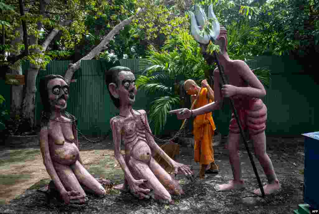 A Buddhist monk sweeps around statues illustrating the fate of people who do bad deeds in a garden depicting a Buddhist version of hell at the Wat Saeng Suk temple in the Thai coastal province of Chonburi, Thailand.