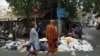 ស្រ្តី​ម្នាក់​និង​ព្រះសង្ឃ​មួយ​អង្គ​ដើរកាត់​គំនរ​សំរាម​នៅ​ក្នុង​រាជធានី​ភ្នំពេញ​មួយ​ថ្ងៃ ​បន្ទាប់​ពី​បុគ្គលិក​​ក្រុម​ហ៊ុន​ស៊ីនទ្រី​មិន​មក​ប្រមូល​​ដើម្បីធ្វើ​បាតុកម្ម​ទាមទារ​ដំឡើង​ប្រាក់​ខែ រាជធានីភ្នំពេញ ថ្ងៃទី​២៦ ខែធ្នូ ឆ្នាំ២០១៨​។ (ទុំ ម្លិះ/VOA)