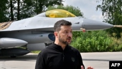 Ukraine's President Volodymyr Zelensky gestures as he speaks to media representatives while standing in front of an F16 fighter jet during Ukrainian Air Forces Day at an undisclosed location on August 4, 2024.