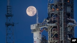 Se ve una luna llena detrás del Sistema de Lanzamiento Espacial Artemis I (SLS) y la nave espacial Orion, encima del lanzador móvil, lista para un ensayo generalen el Complejo de Lanzamiento 39B en el Centro Espacial Kennedy de la NASA en Florida, EEUU, el 14 de junio de 2022. 