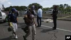Un migrante centroamericano que cayó de la parte trasera de un vehículo en movimiento y murió, yace en una carretera detrás de la policía mientras otros migrantes de la misma caravana caminan en las afueras de Tapachula, México, el lunes 22 de octubre de 2018.