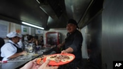 El chef Arturo Rivera Martínez, recién galardonado con una estrella Michelin, entrega una orden de tacos a un cliente en la taquería Tacos El Califa de León en Ciudad de México, el miércoles 15 de mayo de 2024. 