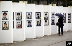 A woman looks at caricatures of the victims of the sunken ferry Sewol outside a group memorial altar in Ansan, South Korea, Thursday, April 16, 2015. Tears and grief mixed with raw anger Thursday as black-clad relatives mourned the 300 people, mostly high school students.