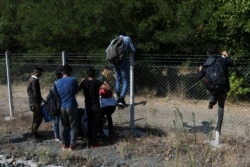 FILE - Migrants jump a fence after reaching the Greek-North Macedonian border on a freight train, trying to cross without documents, near the village of Idomeni, Greece, Aug. 24, 2019.