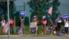 FILE - Supporters hold signs as Republican presidential nominee former President Donald Trump passes in a motorcade en route to a stop at a campaign office in Roseville, Michigan. Aug. 26, 2024.