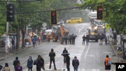 Un grupo manifestantes se mantienen en una barricada cerca del Departamento de Transporte de Seattle, mientras otros trabajadores despejan una barricada a poca distancia.