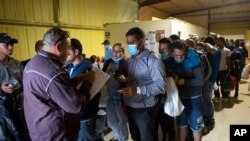 ARCHIVO - Varias personas hacen fila para abordar un autobús que los llevará al aeropuerto de San Antonio en un almacén manejado por el grupo sin fines de lucro Mission: Border Hope, operado por la Iglesia Metodista Unida, en mayo de 2022, en Eagle Pass, EEUU. 