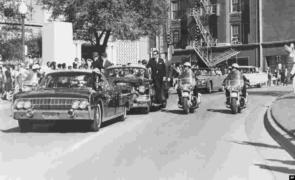 Una vista a través del parabrisas de la limosina mientras recorre la calle Elm pasando el depósito de libros escolares, el presidente Kennedy levanta su mano hacia su cabeza segundos antes de recibir el balazo fatal en Dallas, el 22 de noviembre de 1963. 