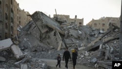 ARCHIVO - Jóvenes palestinos caminan entre los escombros de los edificios destruidos en un barrio de Khan Younis, Franja de Gaza, el 1 de diciembre de 2024.