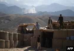 ARCHIVO - Policías afganos miran hacia el horizonte donde una columna de humo se levanta luego de un ataque a posiciones de militantes del Estado Islámico en un punto de control en la oriental provincia de Nangarhar. Julio 7, 2018.