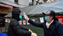 Una mujer revisa la temperatura a un ciclista que porta una mascarilla en la ciudad de Wuhan, en el centro de China, el viernes 21 de febrero de 2020. (Chinatopix via AP)